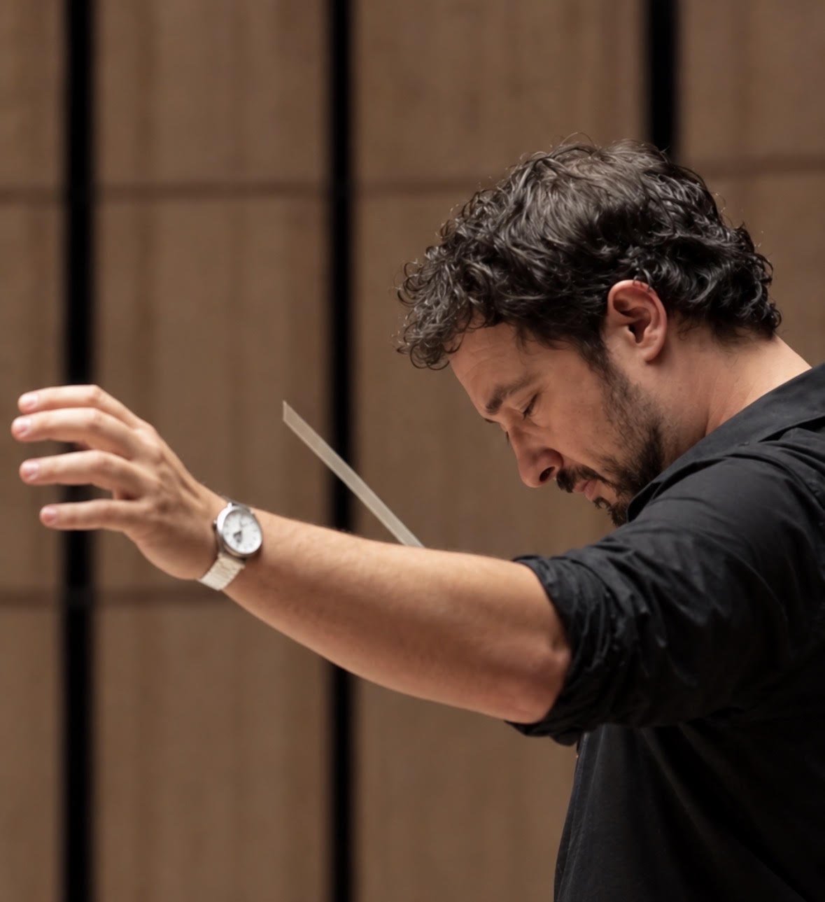 Christian Sebastian conducting, baton raised, eyes lowered toward the score